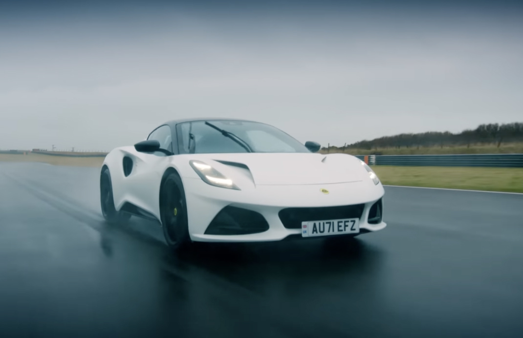 Front angle of a white Lotus Emira driving at speed on a test track in rainy conditions