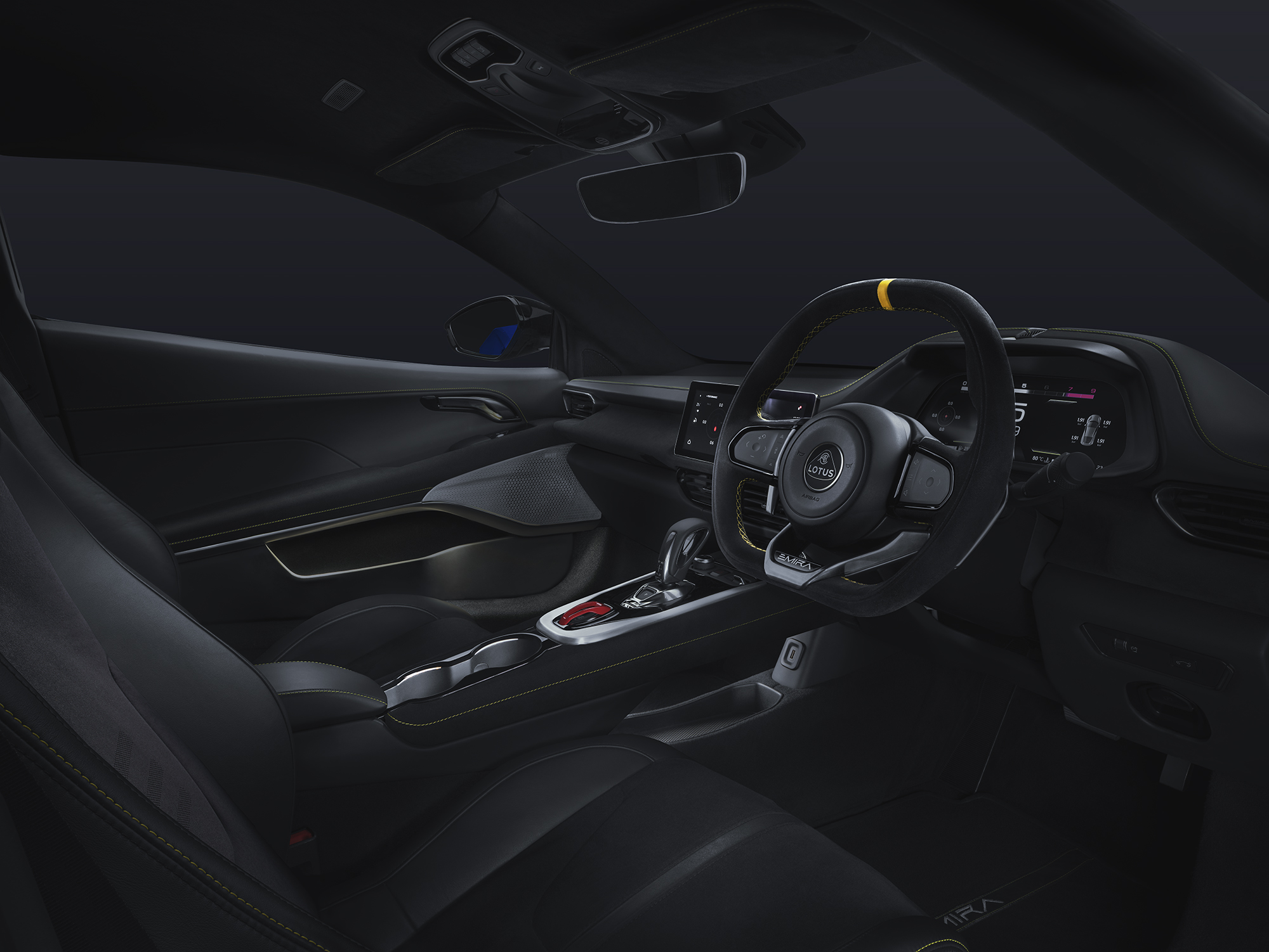 View from the driver's side front window into the Lotus Emira interior. The black and yellow steering wheel, driving display, touchscreen centre console, and metalic controls are all visible. | 0630 Image-1_2000px.jpg