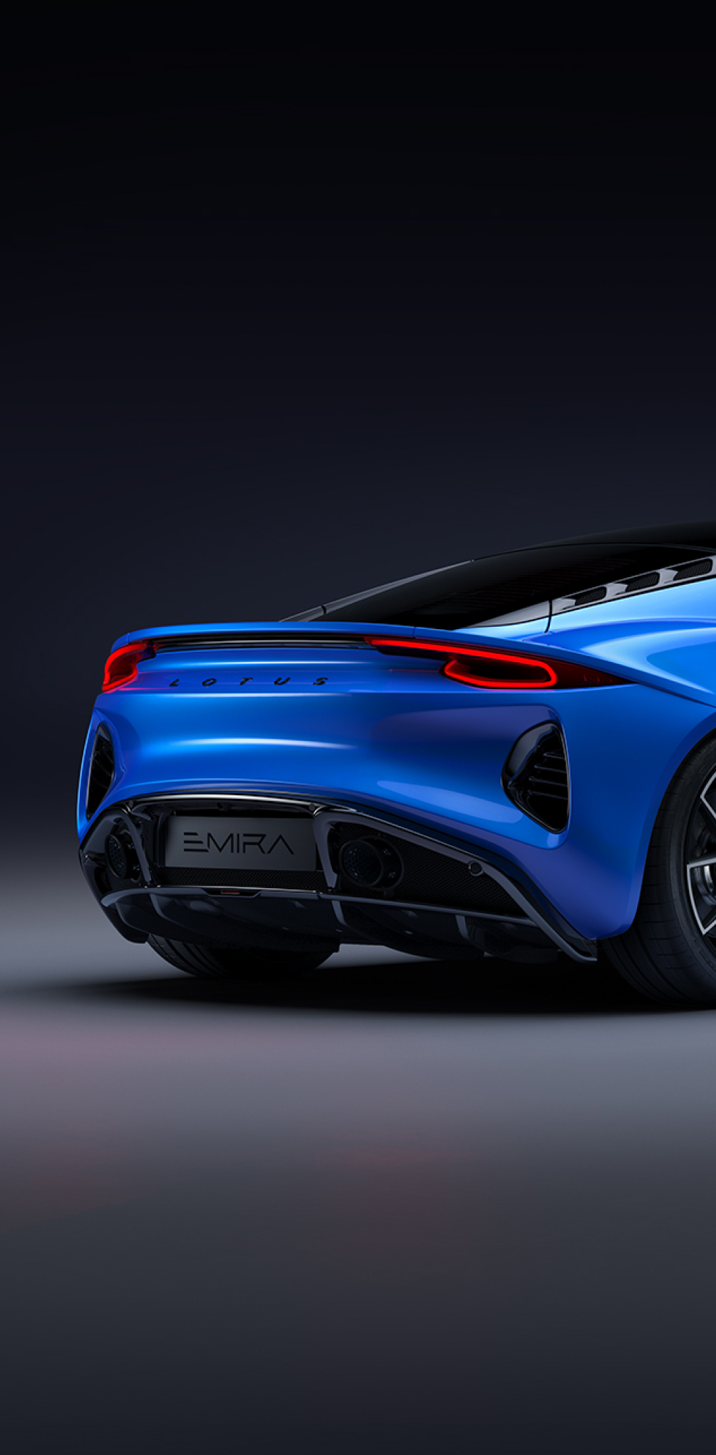 Rear angled shot of a blue Lotus Emira in an abstract grey environment. The rear running lights are glowing red